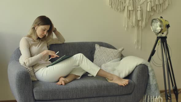 Woman Makes a Business Plan on Tablet Lying on Sofa