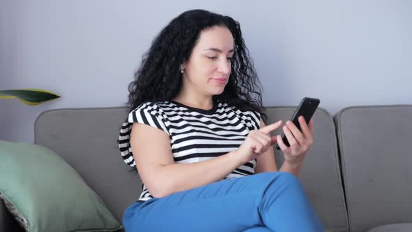 Woman Typing on Phone Sitting on Sofa at Home, Businesswoman Sits at Home Types on Smartphone Checks alt