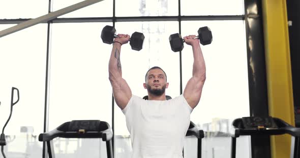 Portrait of a Young Athletic Muscular Man Lifting Heavy Weights Black Dumbbells While Concentrating