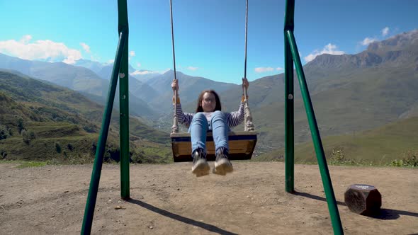 Young Woman Goes for a Drive on a Swing Against a Background of Caucasian Mountains. alt