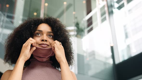 Businesswoman Putting On Face Mask In Modern Open Plan Office During Covid-19 Pandemic alt