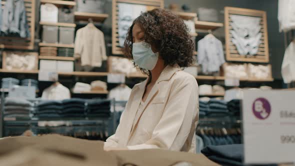 Young Asian woman wearing a medical face mask chooses clothes in a clothing store