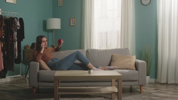 Girl with Red Apple Lies on Sofa and Talks on Phone