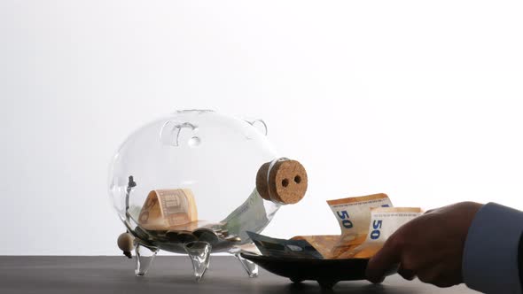 Taking Care of Own Money - a Man Places a Food Bowl Full of Banknotes in Front of a Glass Piggy Bank