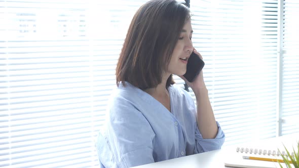 Beautiful young smiling asian woman working on laptop while sitting in a living room at home. alt