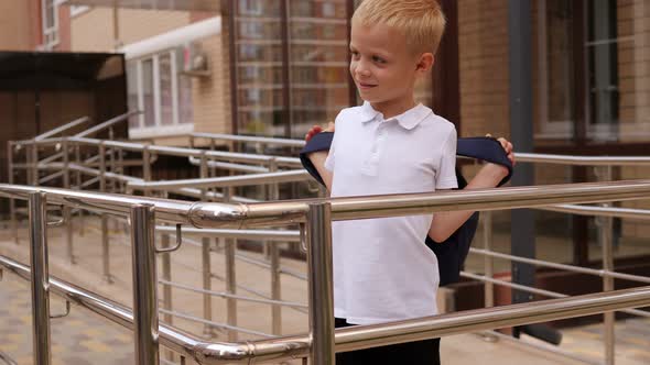 Portrait of a Little Boy Who Puts on a Backpack in the School Yard alt
