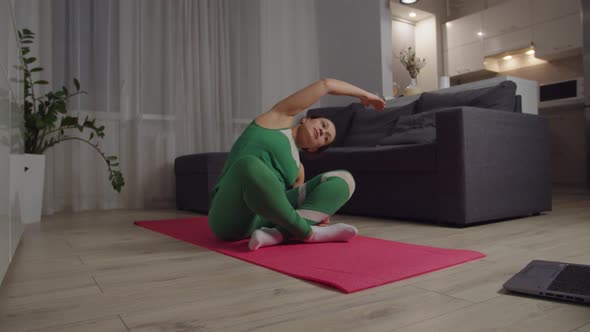 Woman Practicing Side Bending Exercise Sitting on Yoga Mat Indoors alt