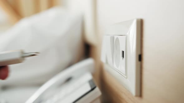 Plugging Power Cord Cable Gadget Charger Charts Into Electric Socket on Wall alt