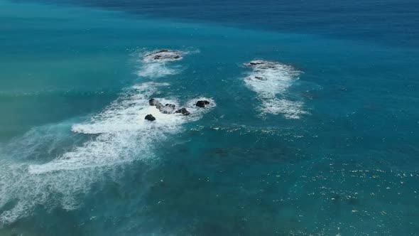 Wide angle, high altitude view of waves breaking and crashing over large rocks near the shoreline. C alt