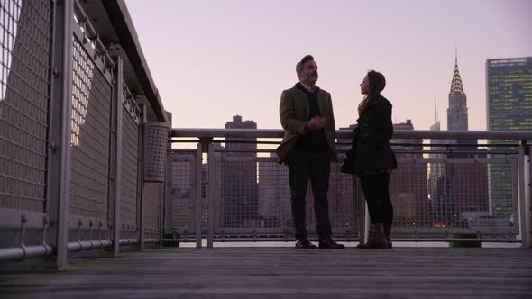 Couple in New York City standing on pier with city skyline in background