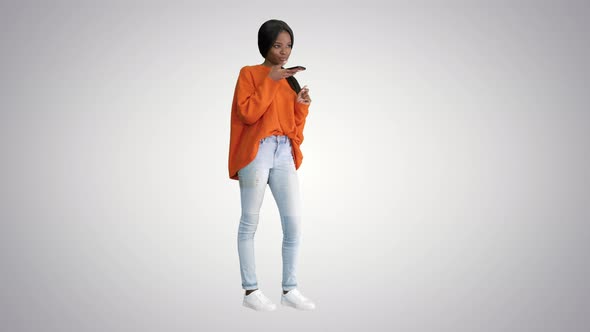 Pretty African American Woman in Bright Jumper Dictating Message Using Her Phone on Gradient alt