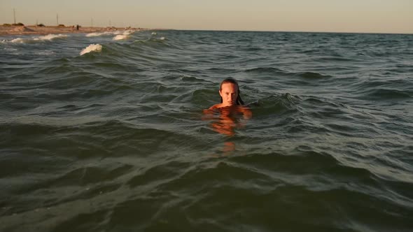 Young Sexy Woman Swims in the Sea on Big Waves in Bikini Swimwear at Sunset alt