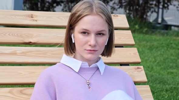 Melancholic Lady Student Listens to Music Sitting on Bench alt