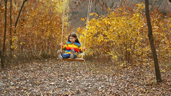 A little girl riding on a rope swing in the autumn Park.