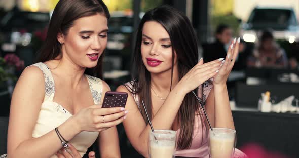 Two Beautiful Girls Drinks Coffee in the Summer Cafe and They Are Surprised