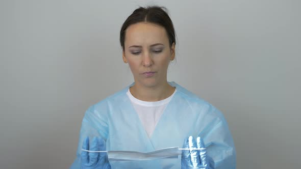 Woman in doctor uniform and surgical blue gloves putting on protection mask preparing for surgery alt