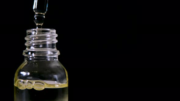 Dripping Oil From Pipette Into Glass Bottle on Black Background alt
