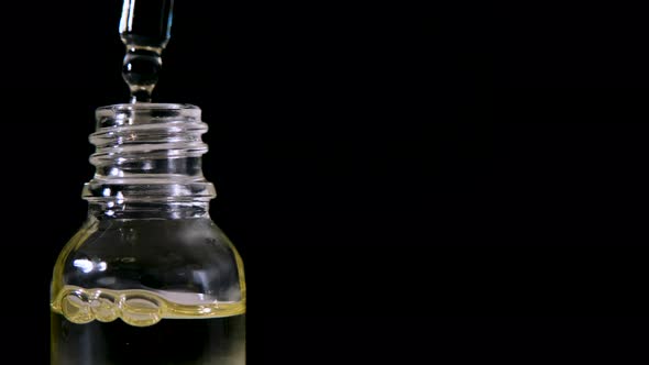 Dripping Oil From Pipette Into Glass Bottle on Black Background