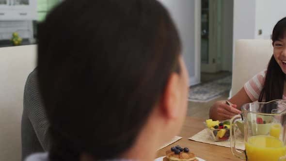 Happy asian parents in kitchen eating breakfast and talking with laughing daughter alt