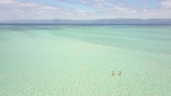 Aerial View of Tourist Couple Walking in the Crystal Clear Shallow Ocean Water. alt