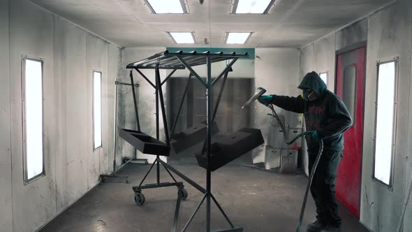 Man applying black anti-corrosion powder coating to metal sheet using a spray gun in factory. alt