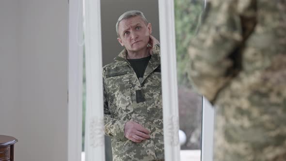 Middle Shot Reflection in Mirror of Serious Army Man Standing at Home Indoors alt