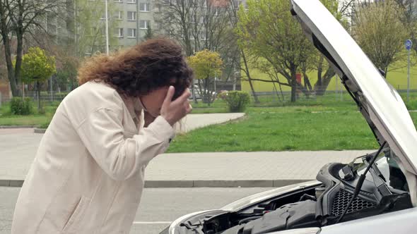 Middleaged Woman Driver Stands Near the Open Hood of Her Car