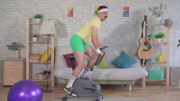 Funny Active Athlete From the 80s with a Mustache Engaged at Home on a Stationary Bike Slow Mo alt