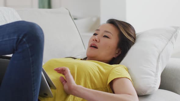 Happy asian woman lying on sofa, resting with laptop at home alt