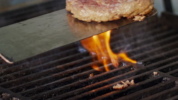 Slow motion of beef hamburger on a grill in close up with flames and smoke alt