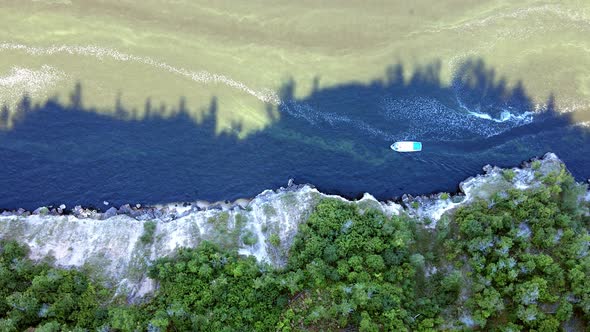 Under the canopy of a sheer cliff, a pleasure boat floats along the river alt