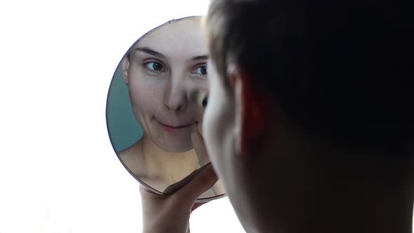 Woman Looking in the Mirror and Apply Makeup to the Face.