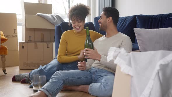 Couple In New Home Celebrate With Champagne Sitting On Floor In Lounge On Moving Day Boxes