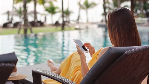 Young woman traveler relaxing and using a mobile phone by a hotel pool