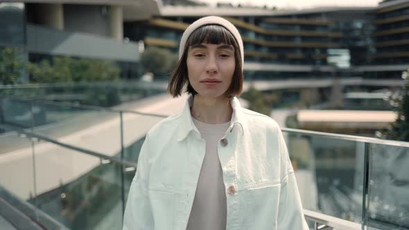 Pleasant Young Lady Holding Smartphone in Hands and Looking to the Camera Standing Near Modern alt