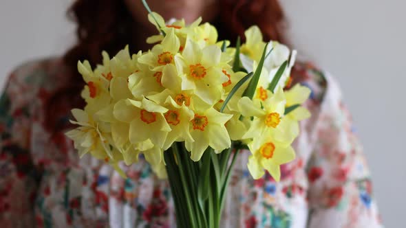 Portrait of Young Romantic Woman Smelling Spring Yellow Daffodils Flowers in Bouquet at Home
