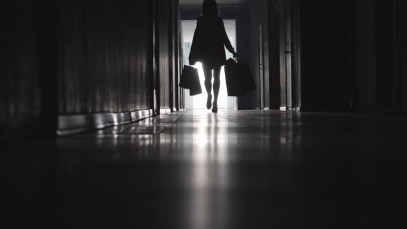 Silhouette of Stylish Lady Going with Shopping Bags along Hallway