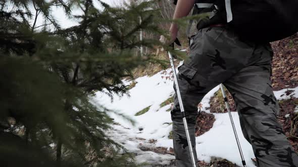 Backpacker in hiking gear with trekking poles walking up outdoor trail with snow. Slow motion alt