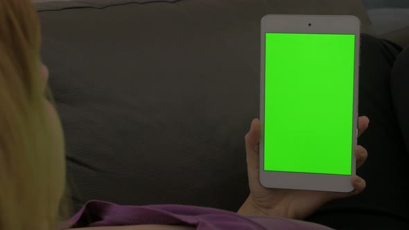 Young woman relaxing on bed while looking to greenscreen display on silver tablet 4K 3840X2160 UHD v
