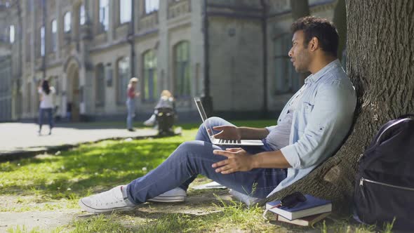 Mixed-Race Young Guy Using Laptop Under Tree, Getting Bad News, Disappointment alt