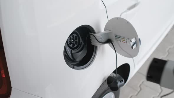 Woman Inserts a Power Cord Into an Electric Car for Charging alt