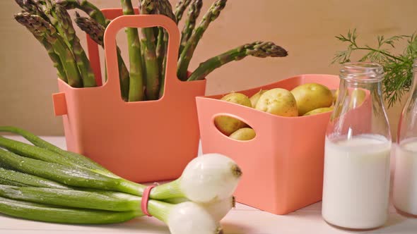 Spring Young Vegetables in Coral Containers and Bottles with Milk on Table alt