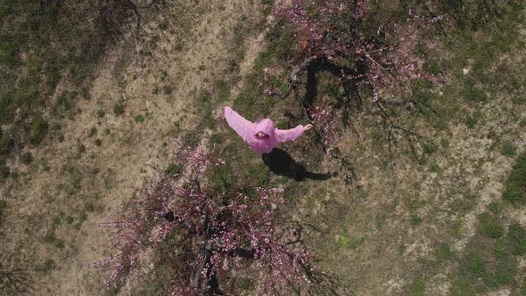 Woman in a Pink Hooded Dress with Flowers Walks Through a Peach Field alt