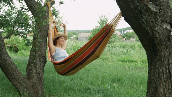 Young cute brunette girl resting on hammock, unwinds on hammock in countryside. alt
