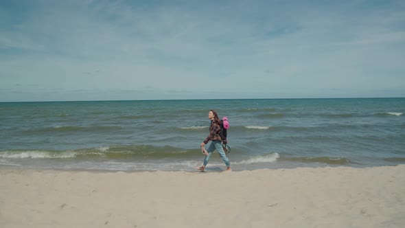 Female tourist with backpack walking along sea beach