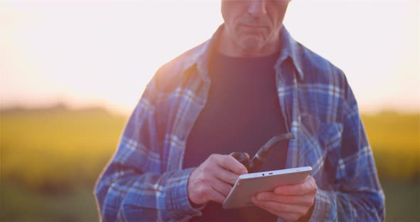 Farmer Examining Agricultural Field While Working on Digital Tablet Computer at Farm. alt
