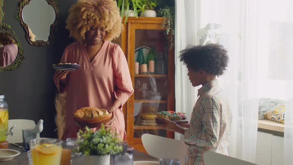 Mother and Little Son Setting Up Table for Family Dinner alt
