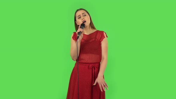 Tender Girl in Red Dress Is Singing Into a Microphone and Moving To the Beat of Music. Green Screen alt
