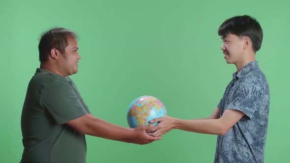 Asian Man Hand In The World Globe To Adult Man While Standing In Front Of Green Screen Background alt