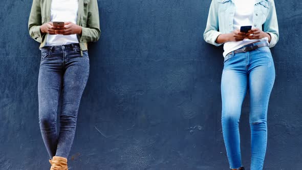 Twin sisters using mobile phone on a sidewalk in the city 4k alt